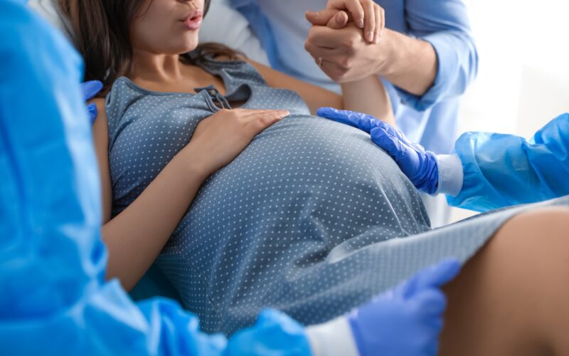 tehotná žena v modrej košeli je v pôrodnici, počas pôrodu, lekári v modrých gumených rukaviciach okolo nej