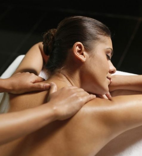 Žena leží na bruchu a užíva si relaxačnú masáž ramien a hornej časti chrbta v pokojnom prostredí.